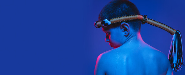 Young boy thai boxer posing over blue background in neon light.