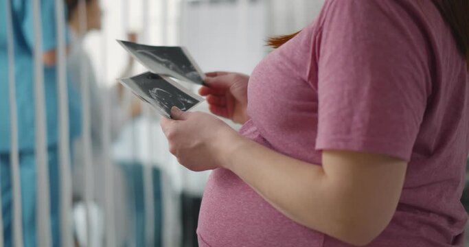 Cropped shot of pregnant woman touching belly and holding sonogram picture