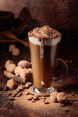 Glass of hot chocolate with whipped cream and truffles on an old brown table.
