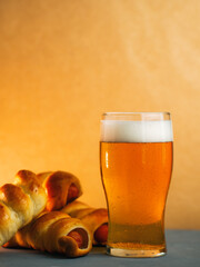 A glass of light beer on the table, sausages in the dough appetizer. Yellow background.