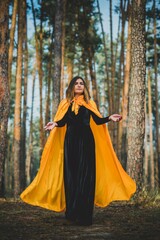 Fototapeta premium Mysterious woman in cape at wood. Illustration to Halloween or other scary story
