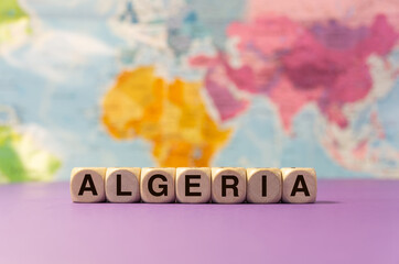 The word Algeria written with wooden dices in front of a purple background and a geographic map