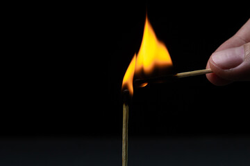 Burning match on a black background. A match sets fire to another match against a dark background....