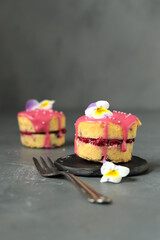 kleine Napfkuchen mit Himbeerfüllung und Himbeerglasur, dekoriert mit Zuckerperlen und Hornveilchen