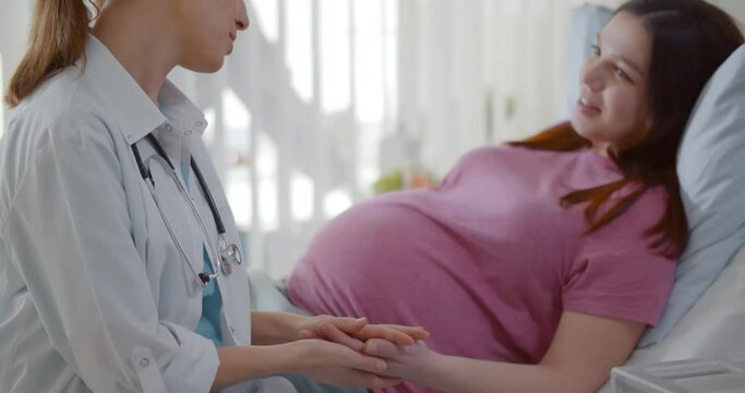 Doctor supporting and holding pregnant woman hand in hospital ward