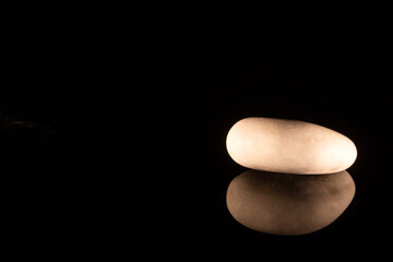 Fototapeta na wymiar A white pebble lying on a black reflective surface