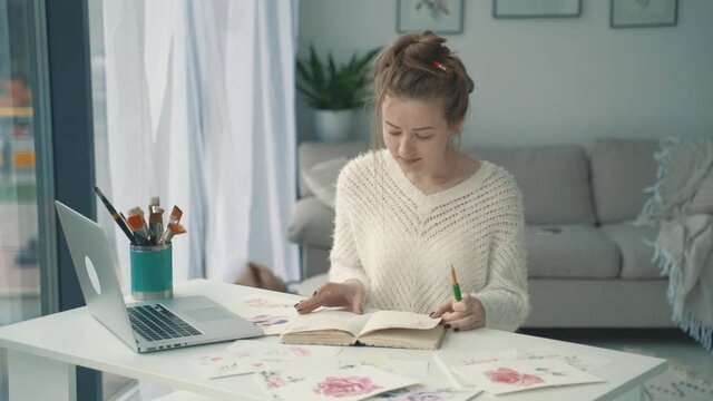Streamer at home. Young female artist with a notebook of illustrations and a laptop.