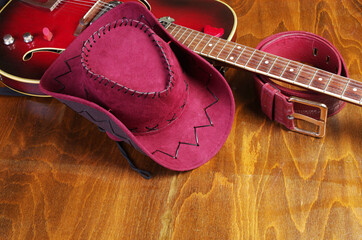Cowboy set. Electric guitar, cowboy hat and leather belt on a wooden table.