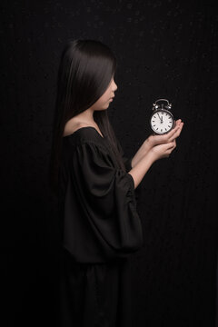 It is time to wake -up; conceptual classic portrait of a girl en profile in black holding a clock; five before twelve o'clock 