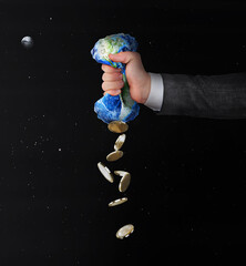 Ecological concept. A human hand squeezes the planet like a sponge, extracting resources against...