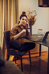 A beautiful pregnant businesswoman sitting at the dining table and working from home.