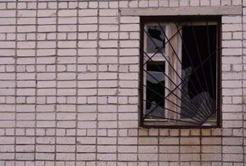 Fototapeta na wymiar A broken window in a brick house. Broken glass in a window with a metal grate.