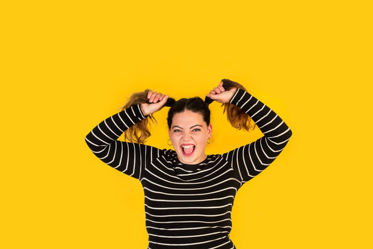 Mujer joven gritando y tirandose de los pelos sobre un fondo amarillo brillante liso y aislado. Vista de frente. Copy space