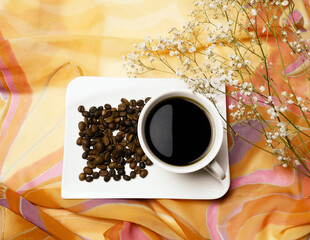 Cup of hot coffee and coffee beans on orange background
