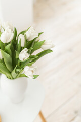 White tulips stand in a vase in a beautiful room. Spring mood in the interior.