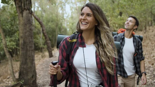 Couple of happy hikers looking around, admiring landscape, carrying camping backpacks, walking on forest path, talking, enjoying outdoor vacation and healthy recreation. Adventure travel concept