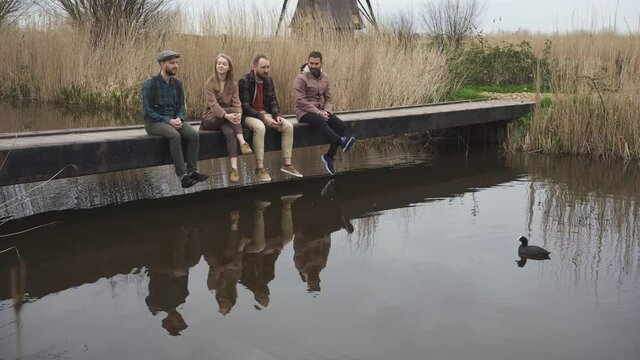 Group of Four Cheerful Friends are Feeding Ducks Sitting on the Bridge in Kinderdijk, Netherlands at Spring