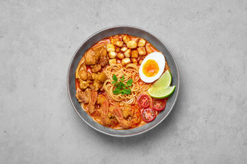 Laksa in gray bowl on concrete table top. Coconut noodle soup with chicken meat and prawns of peranakan cuisine. Asian food.