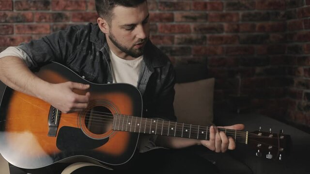 Young musician man playing guitar and singing at home