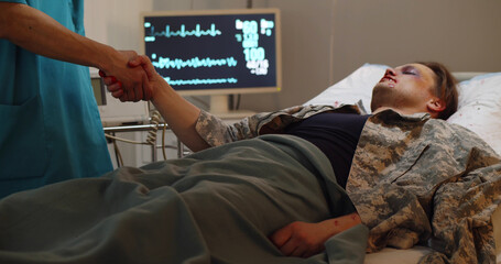 Injured soldier lying in hospital and shaking hands with doctor