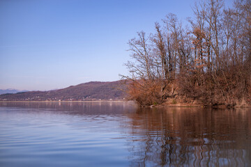 Fototapeta premium landscape with a huge lake at the end of the autumn season. rocky mountains and high forests on the distant horizon. silhouettes of leafless trees reflected in the luster of the water