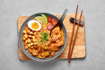 Laksa in gray bowl on concrete table top. Coconut noodle soup with chicken meat and prawns of peranakan cuisine. Asian food.