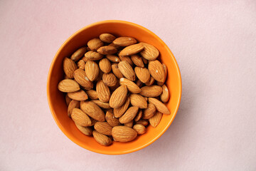 Bowl of fresh almonds on color background, top view