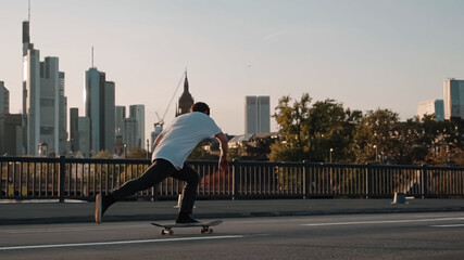 skateboarder pushing on bridge in front frankfurt skyline skyscrapers sunset