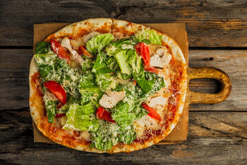 Pizza with caesar salad. Chicken meat, tomatos, lettuce, sauce, grated cheese, on wooden board, rustic wooden backdrop