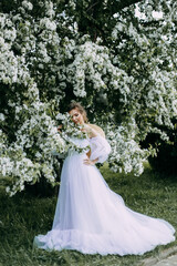 Obraz na płótnie Canvas Portrait of a beautiful inspired sweet romantic gentle pretty bride a young woman in a wedding dress walking and standing alone in a blooming spring green park, selective focus