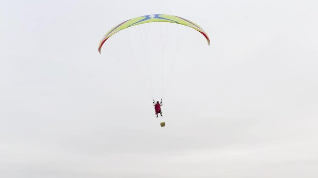  Beginning of paragliding, instructor with a red Superman cloak and client rising into the air. Action. Paragliders soaring on cloudy sky background.