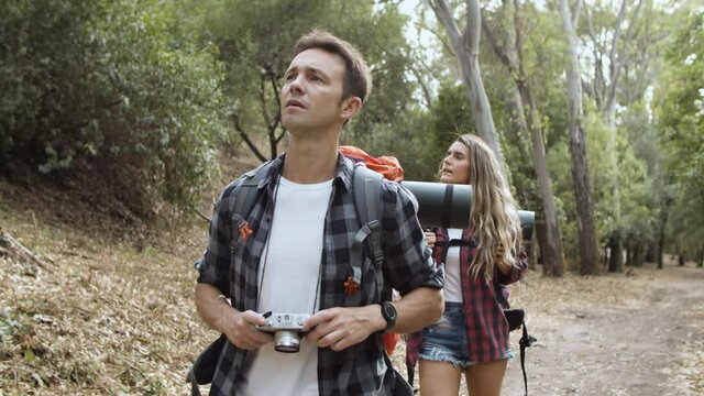 Couple of hikers with photo camera taking pictures of landscape while walking on forest path, enjoying outdoor vacation and healthy recreation. Adventure travel concept