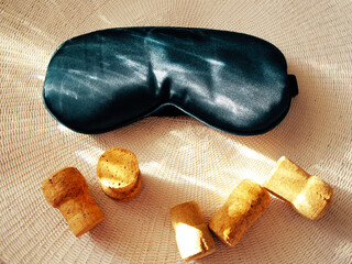 A soft cloth sleep mask and wine bottle corks are set against a light woven background. The concept...
