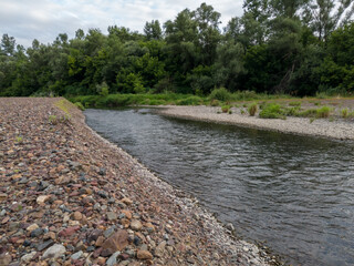 Landscape of river Ukrine, fast water current eroding gravel shore, riverbank overgrown with green...