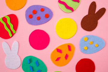 Abstract picture of cut out of felt applications of colourful eggs and white and brown rabbits. Pink background. Flat lay. Easter holiday