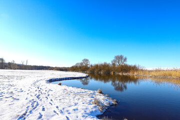 Winter river, panoramic view of the picturesque winter-spring landscape at sunrise. Bright blue sky, frozen shore, snow, ice.