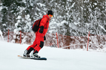 Male snowboarder in a red suit rides on the snowy hill with snowboard, Skiing and snowboarding...