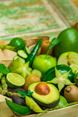 Avocado among other fruits and vegetables in crate on rustic, vintage exfoliating painted wood