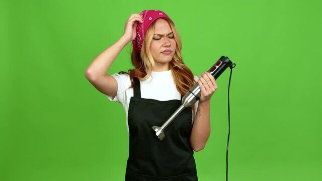 Young blonde girl using hand blender having doubts while scratching head over isolated background over isolated background on green screen chroma key background 