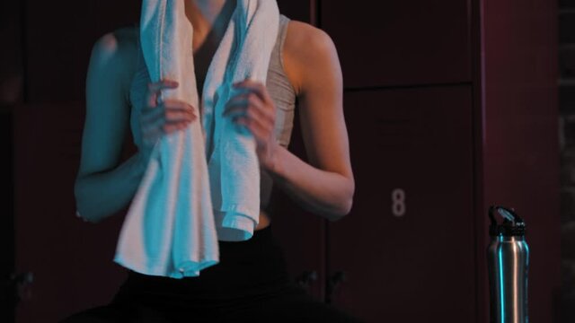 A young woman sitting in locker room - putting a towel on her neck - looking in the camera