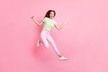 Full length portrait of charming young girl jumping high toothy smile raise hands palms isolated on pink color background