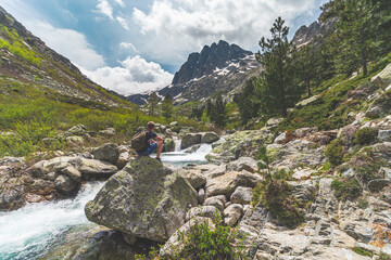 Hiker sits on the rock in mountainous river valley in Corsica national park