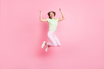 Fototapeta na wymiar Full size photo of cheerful carefree young girl jumping fists up celebrate isolated on pink color background