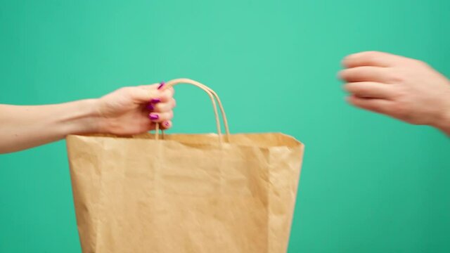 Courier in gloves passing craft shopping bag with delivery against mint background