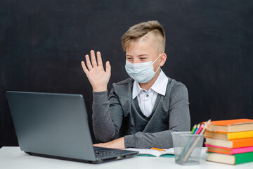 Teen boy wearing mask uses laptop at school near blackboard during corona virus and flu outbreak