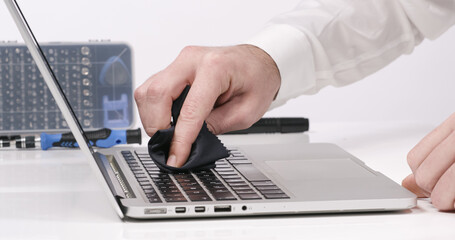 Service worker cleaning laptop keyboard buttons with microfibre cloth in white walled lab