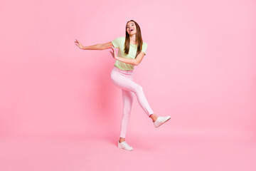 Full length photo of adorable funny young lady wear green t-shirt dancing isolated pastel pink color background