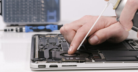 Service worker repairing cleaning dust laptop motherboard circuit board cooler with compressed air in white walled lab