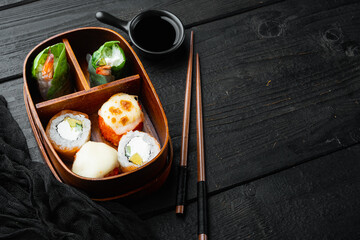 Fresh Food Portion in Japanese Bento Box with Sushi Rolls, on black wooden table background , with copyspace  and space for text