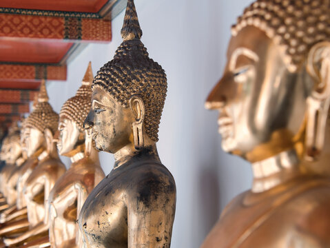 golden Buddha statues in a temple in Bangkok, arranged in a row. Focus on statue in the center of the image